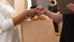Pessoa entregando uma sacola de papel para um cliente, simbolizando uma compra ou troca em um ambiente comercial.