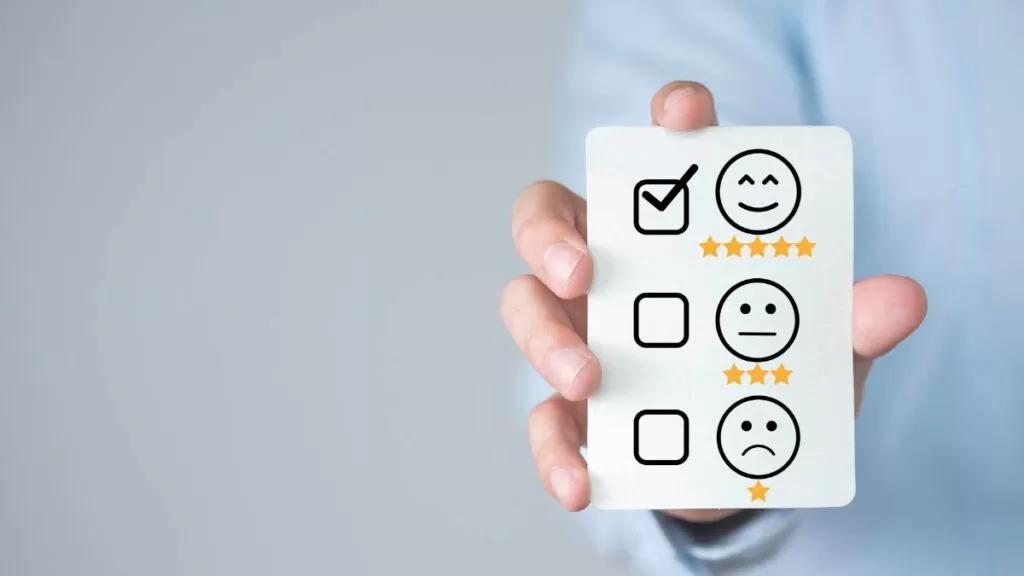 Mão segurando um cartão com carinha sorridente e estrelas, simbolizando o nível satisfação do cliente